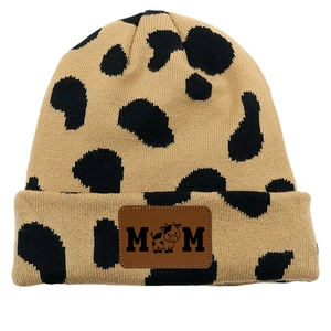 Detailed close-up of cow print knit beanie featuring a brown leather MOM logo patch