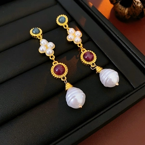 Detailed view of vintage gold earrings with colorful gems and baroque pearls on black tray
