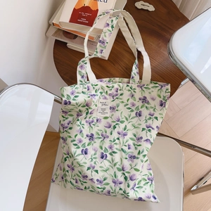 Borsa tote in cotone bianco con stampe floreali viola, mostrata su una sedia moderna