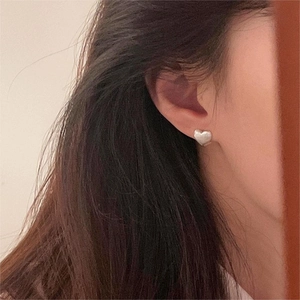 Close-up of minimalist brushed S925 sterling silver heart stud earrings worn on ear