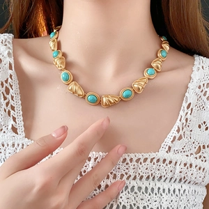 Détail d'un collier vintage doré avec pierres vertes porté sur de la dentelle blanche