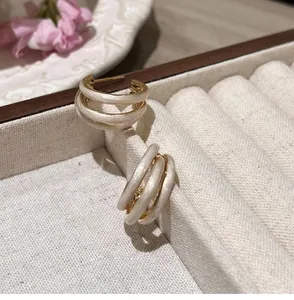 Detail view of triple-layered C-shaped earrings with cream enamel and gold plating finish