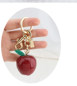 Close-up of a sparkling dark red apple keychain with green leaf on a metal ring