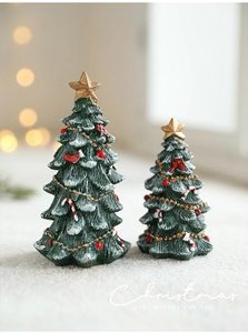 Detail of two resin green snow-covered Christmas trees with gold and red ornaments