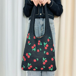 Close-up of black knit tote bag featuring red cherry patterns held by a model