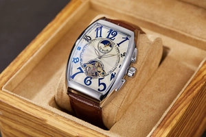 Detail of tonneau mechanical watch with silver case and brown leather strap in wood box
