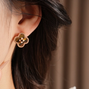 Close-up of golden four-leaf clover earring with tiger eye stones and pearls on ear