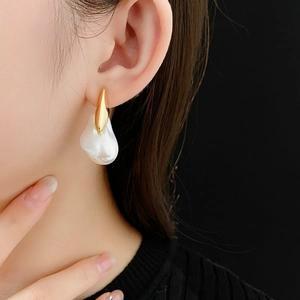 Detail of gold-plated earrings with irregular baroque pearl drop worn by a model