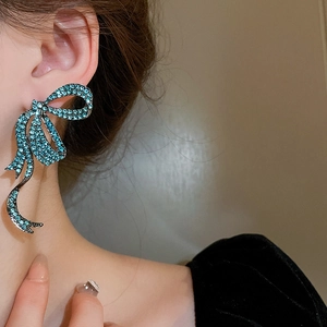 Close-up of elegant bow earrings with deep blue rhinestones worn in a stylish setting