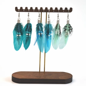 Detailed view of three pairs of bohemian feather drop earrings on a wooden display stand