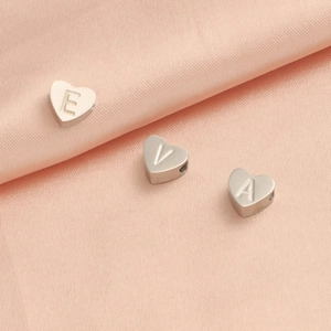 Vue macro de perles lettres en forme de cœur en acier inoxydable sur soie rose