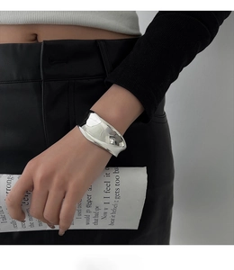 Detailed view of an irregular wide silver bangle worn with minimalist fashion styling