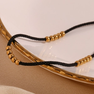 Close-up of black braided anklet featuring twenty-five 18K gold-plated steel beads
