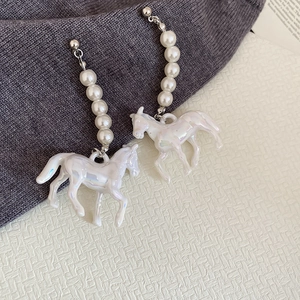 Détail de boucles d'oreilles cheval argentées avec perles blanches sur fond texturé