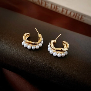 Detailed view of gold C-shaped layered pearl earrings on a vintage French book background