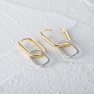 Detail view of gold and silver S925 sterling silver curved wave hoop earrings on stone
