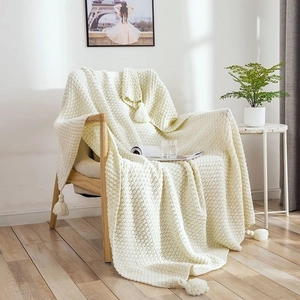 Detail of cream white knit throw blanket with fringe tassels on a wooden armchair