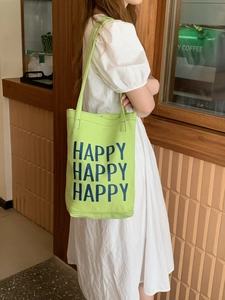 Detail of green canvas tote bag with Happy prints worn by a model in a casual setting
