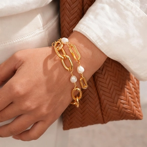 Model wearing a thick gold-plated link chain bracelet with baroque pearls on her wrist