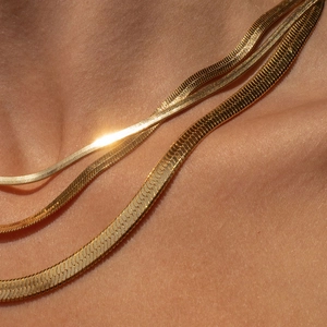 Close-up of layered gold snake chain necklaces with polished flat metal textures
