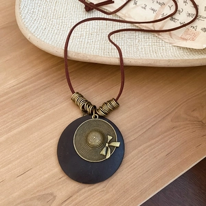 Macro shot of retro wood circle pendant with bronze hat detail on brown leather cord