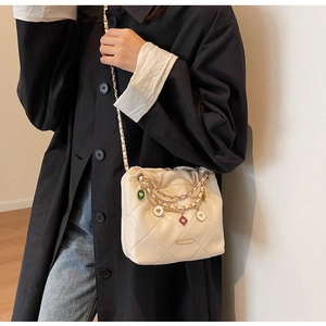 Detail of cream quilted bucket bag featuring gold chain and colorful enamel charms