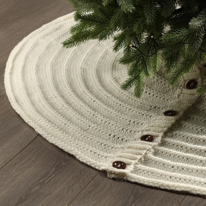 Off-white chunky knit Christmas tree skirt with wooden buttons on dark wood floor