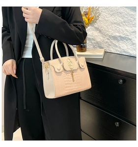 Detail of light beige crocodile embossed handbag with gold hardware and tassel charm