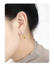 Detail of silver rectangular ear buckle with gold heart pendant worn on ear