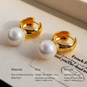 Golden chunky hoop earrings featuring large white Mabe pearls on cream textured fabric