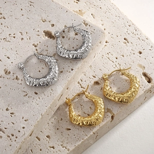 Detail of gold and silver C-shape earrings with a hammered texture on stone background