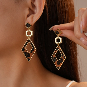Detail of leopard print geometric earrings featuring gold hardware on a model