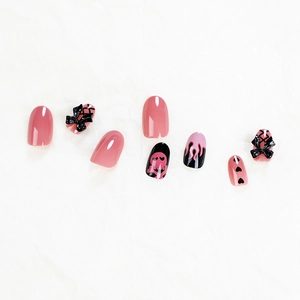 Pink and black flame press-on nails set with 3D bows and skull patterns on white surface