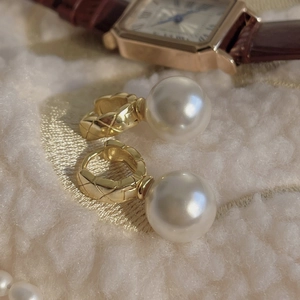 Detail of 925 silver pearl drop earrings with golden quilted pattern on luxury fabric