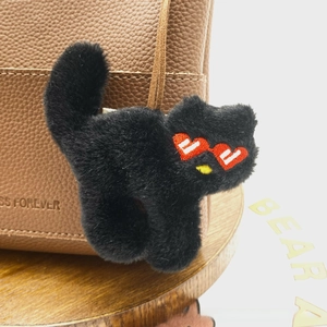 Macro shot of a black plush cat charm with red heart sunglasses embroidery on a leather bag