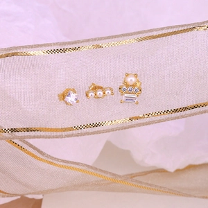 Detailed view of three gold earrings featuring white zircon and elegant pearls