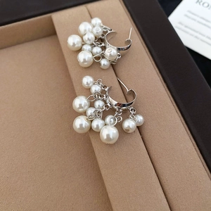 Detail of C-shaped pearl tassel earrings with silver finish and lustrous beaded drop