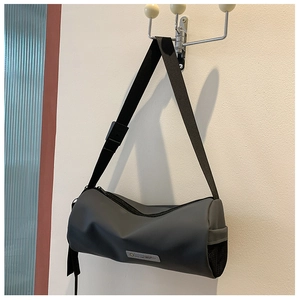 Détail d'un sac bandoulière cylindrique gris foncé suspendu au mur avec texture