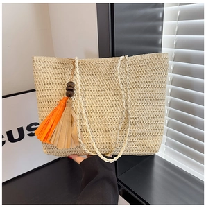 Detail of straw woven tote bag featuring orange and beige tassels with wooden beads