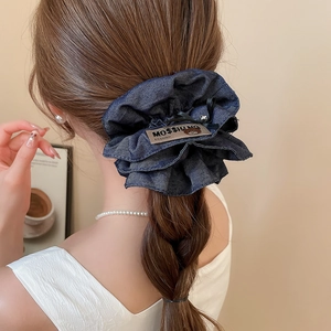 Close-up of a blue denim scrunchie with layered ruffles and a decorative bear motif