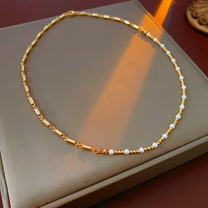 Detailed view of necklace with gold cylindrical tubes and white round pearls on gray mat