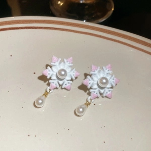 Détail de boucles d'oreilles flocon avec pompons roses et perles sur plat céramique