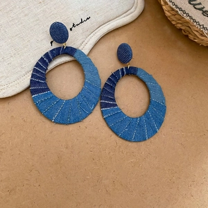 Close-up of denim fabric hoop earrings with frayed edges and golden metal connector