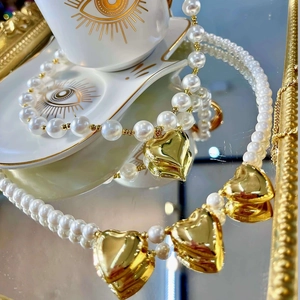 Lustrous pearl necklace with gold heart charms displayed on a reflective mirror surface