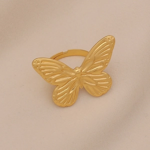 Close-up of golden butterfly open ring with detailed wing textures on beige background