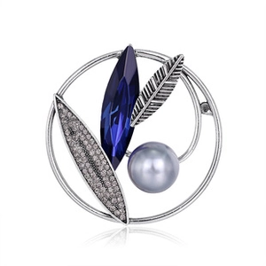 Detail of alloy brooch with blue crystal, grey pearl and rhinestone leaf on white base