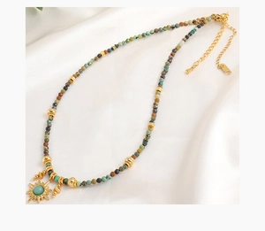 Detail of colorful natural stone beads with gold sun pendant on white silk fabric