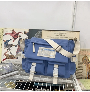 Close-up of blue messenger bag with white buckles and adjustable shoulder strap on shelf