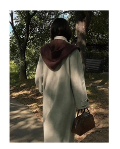 Outdoor back view of a light green hooded shawl scarf with a contrasting brown hood