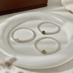 Close-up of white pearl bracelets featuring a central green jade bead and gold spacers
